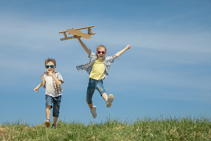 Little kids playing with cardboard toy airplane in the park at t